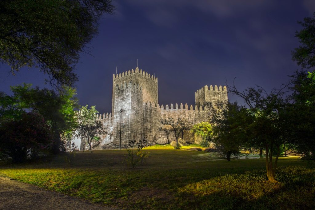 a castle lit up at night with trees in the foreground Guimarães