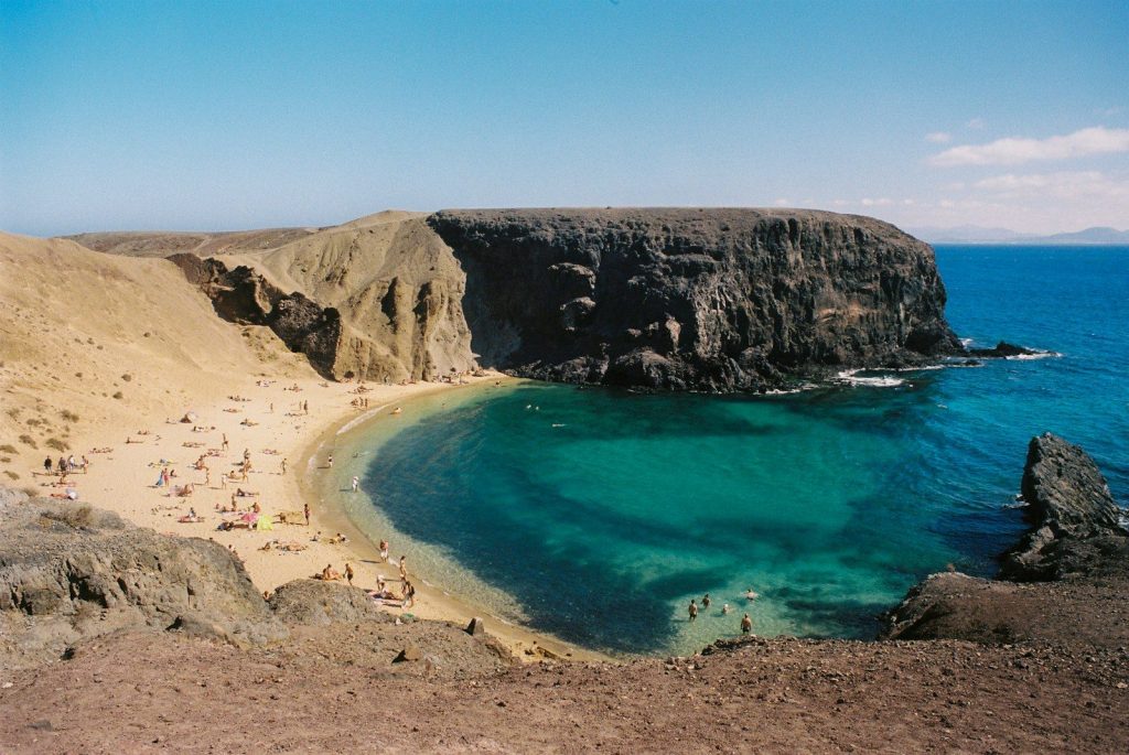 waar is het warm in oktober in europa
a sandy beach with clear blue water next to a cliff