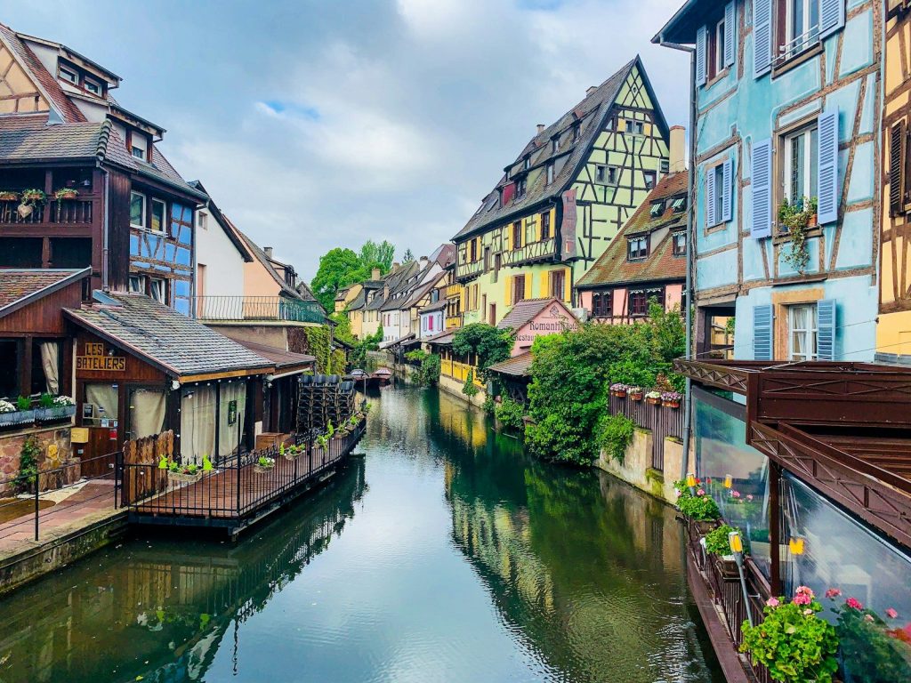 brown and white concrete buildings beside river under white clouds during daytime colmar